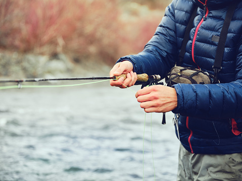 An Asian Korean man, fly fishing on the Provo River in Utah during winter.