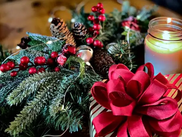 Photo of Festive holiday background of decorated pine boughs and part of present near lighted scented candle on tabletop - stock photo