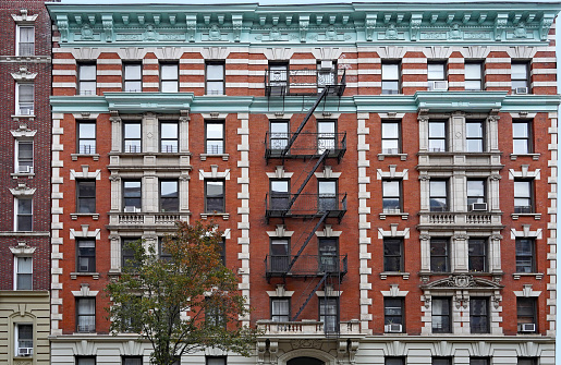 Old fashioned Manhattan apartment building facade with ornate roof cornice and external fire escape ladders