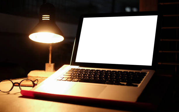 istock Mock up computer laptop with empty display and glowing lamp on wooden table in dark room. 1355019631