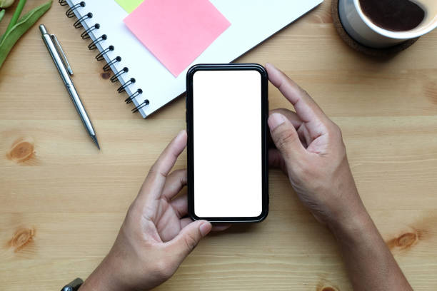 istock Young man holding smart phone with blank screen on wooden table. 1355019634