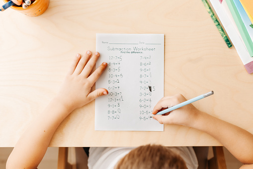 Top view of child hands with pencils. Solving maths exercises. 7 years old child doing maths lessons sitting at desk in his room.