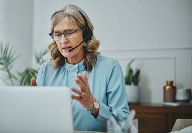 foto de una mujer madura usando un auricular y una computadora portátil en una oficina moderna - on the phone caucasian business mature adult fotografías e imágenes de stock