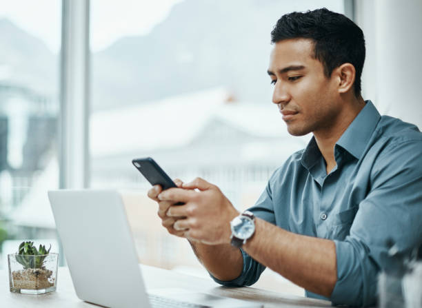 aufnahme eines jungen geschäftsmannes mit smartphone und laptop in einem modernen büro - smart phone business person computer businessman stock-fotos und bilder