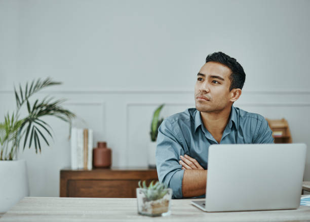 photo d’un jeune homme d’affaires utilisant un ordinateur portable dans un bureau moderne - technology contemplation clothing formalwear photos et images de collection