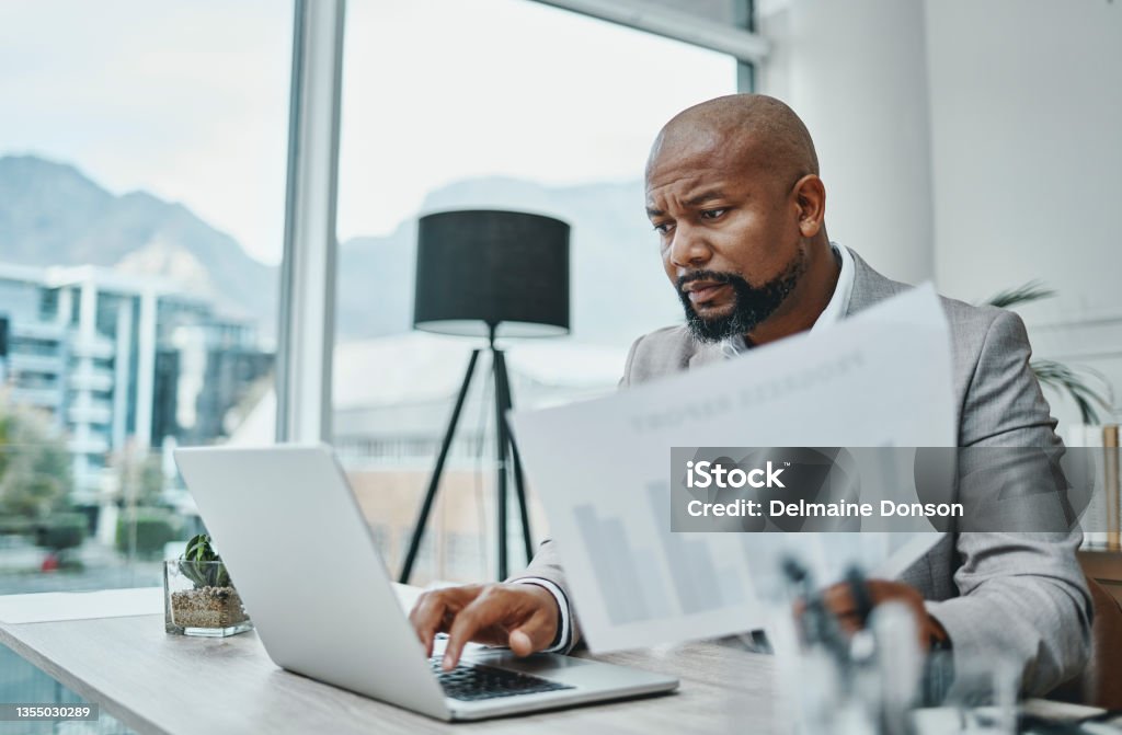 Shot of a mature businessman using a laptop and going over paperwork in a modern office The number crunching king Audit Stock Photo