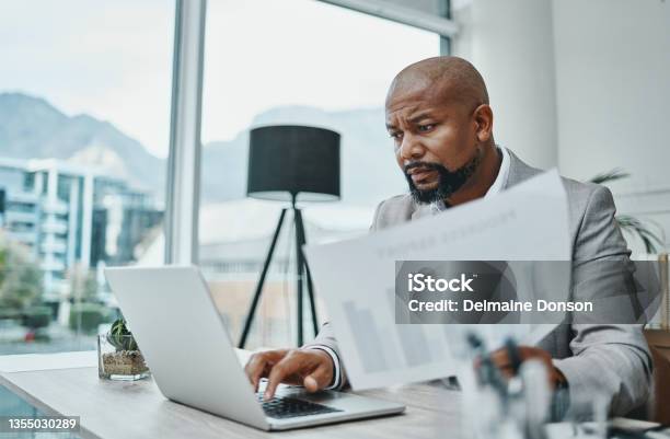 Shot Of A Mature Businessman Using A Laptop And Going Over Paperwork In A Modern Office Stock Photo - Download Image Now