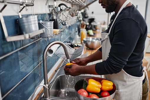 Side view portrait of African-American man washing fresh vegetables while cooking in kitchen, copy space