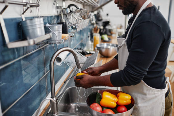 Man Washing Vegetables in Sink Side view portrait of African-American man washing fresh vegetables while cooking in kitchen, copy space commercial kitchen photos stock pictures, royalty-free photos & images