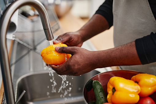 Close up of African-American man washing fresh vegetables while cooking in kitchen, copy space