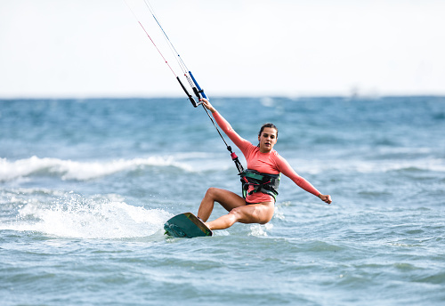 Athletic woman having fun while kitesurfing on the sea during summer vacation.