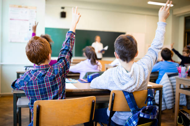 des écoliers en classe avec les mains levées répondant à la question de l’enseignant. - écolier garçon photos et images de collection