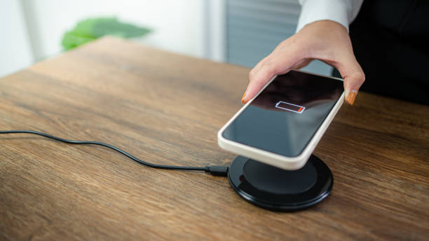 istock Charging mobile phone battery with wireless charging device in the table. Smartphone charging on a charging pad. Mobile phone near wireless charger Modern lifestyle technology concept. 1355040598