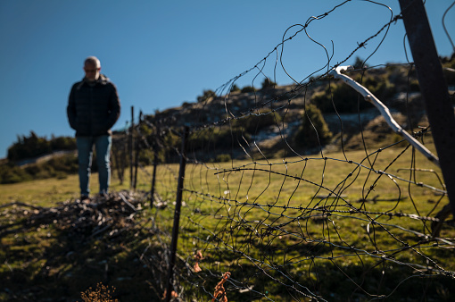 Wire fence in field with adult man in background. In Guadalajara, Castilla La Mancha, Spain