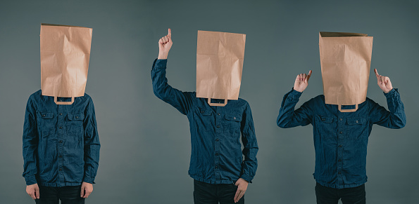 Three young men with paper bags on the head, different positions of the hands, copy space, dark background