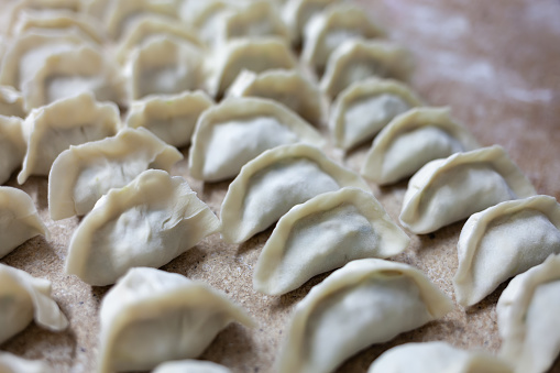 Horizontal shot of an anonymous chef's hands filling dumplinggyoza wrappers on a wooden plate