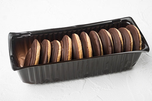 Chocolate coated biscuit cakes set, in plastic tray container, on white stone table background