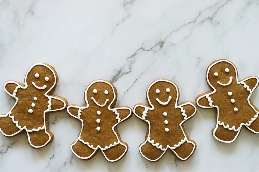 Stock photo showing elevated view of marble effect background with batch of homemade gingerbread men decorated with white, royal icing.