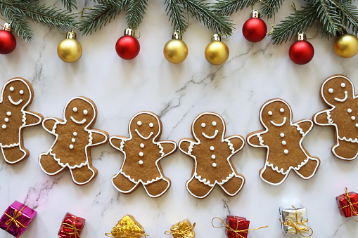 Stock photo showing elevated view of marble effect background with batch of homemade gingerbread men decorated with white, royal icing.