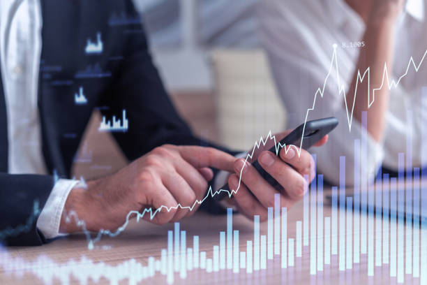 istock Two traders man and woman researching historic data to predict stock market behavior using laptop and phone. Internet trading concept. Forex and financial hologram chart. Forecasting and planning. 1355047215
