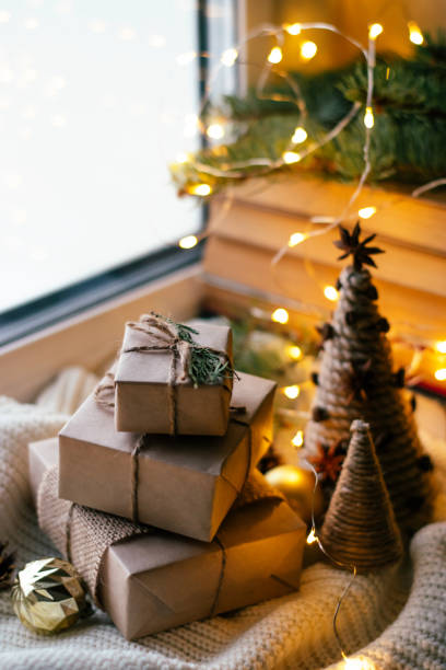 Gift boxes packed in craft paper and a homemade Christmas tree made of thread and cardboard on a festively decorated windowsill.New Year,Christmas and eco-friendly concept. stock photo