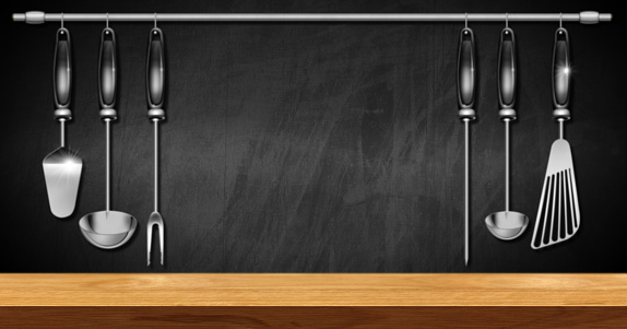 Empty wooden table top with a set of kitchen utensils and a blackboard with copy space on background.