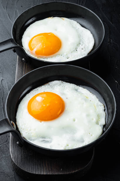 istock Fried eggs with bacon and vegetables in cast iron frying pan, on black background 1355049207