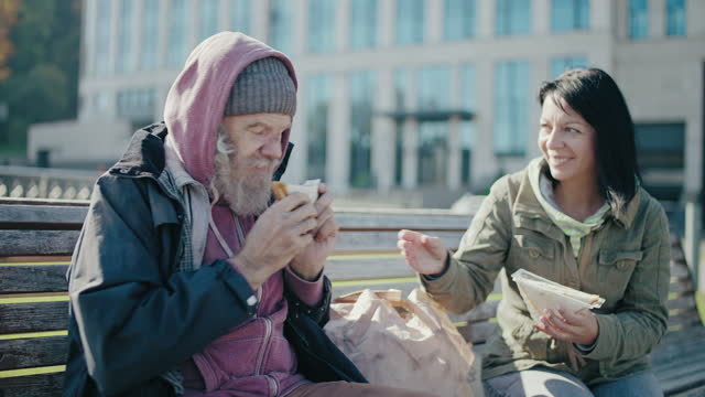 Kind volunteer giving sandwich to homeless man on the bench, urban charity