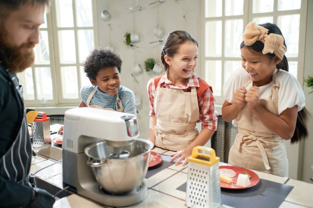 Children learning to cook together Group of happy children laughing during cooking lesson with cook in the kitchen cooking class photos stock pictures, royalty-free photos & images