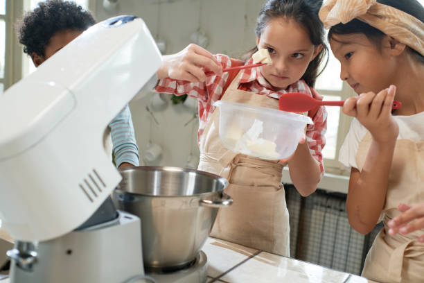 Children making cream for cake in team Group of children adding ingredients in the bowl and making cream for cake together in team during cooking lesson cooking class photos stock pictures, royalty-free photos & images