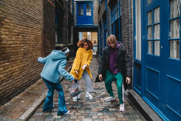 Three happy friends dancing together in the city. Mixed race and african ethnicities. They are wearing cool clothes and dancing in Shoreditch, London.