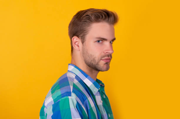 istock Handsome unshaven guy with serious face half turn yellow background, portrait 1355057104