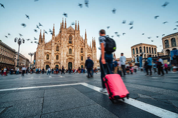 People are visiting Milan, Italy. Blurred motion. A man with a red suitcase in foreground. Milan Cathedral in the background.