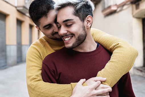 Lgbt gay male couple having tender moment hugging outdoor in the city - Focus on right man face
