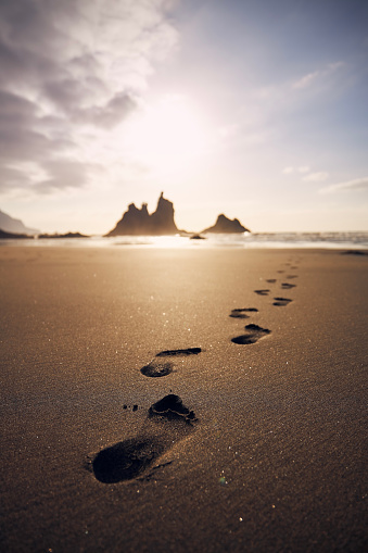 Footprints in sand on beach leading to sea. Golden sunset in Tenerife, Canary Islands, Spain.\