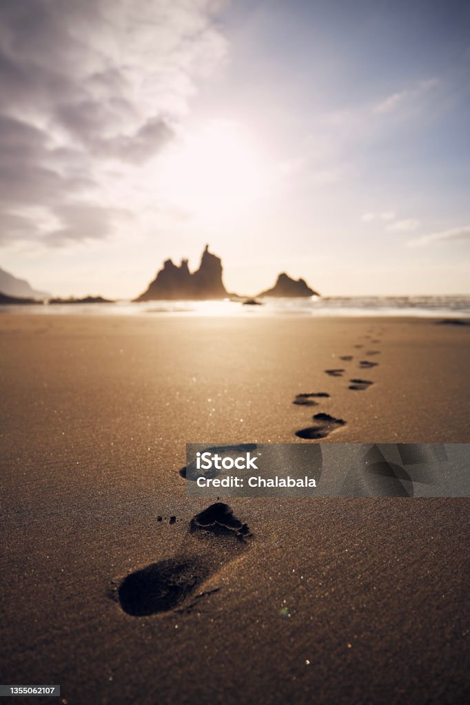 Footprints in sand on beach leading to sea Footprints in sand on beach leading to sea. Golden sunset in Tenerife, Canary Islands, Spain."n Footprint Stock Photo