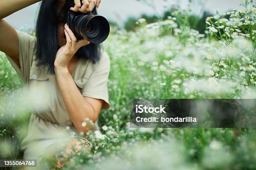 istock Portrait of Female photographer take photo outdoors on flower field landscape holding a camera 1355064768