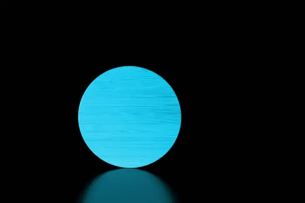 Close-up blue round textured wooden shape on black background with reflection.Low key.Copy space for text.Product placement room.Horizontal banner.Minimalism.Concept of supermoon or sun in darkness.