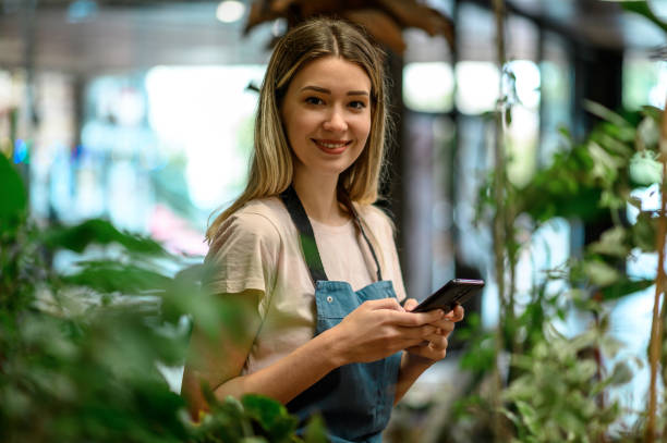 istock Florist using smartphone while surrounded with flowers and plants in a flower shop 1355065680