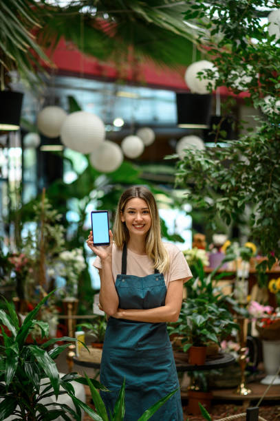 istock Florist showing a smartphone while surrounded with flowers and plants in a flower shop 1355065708