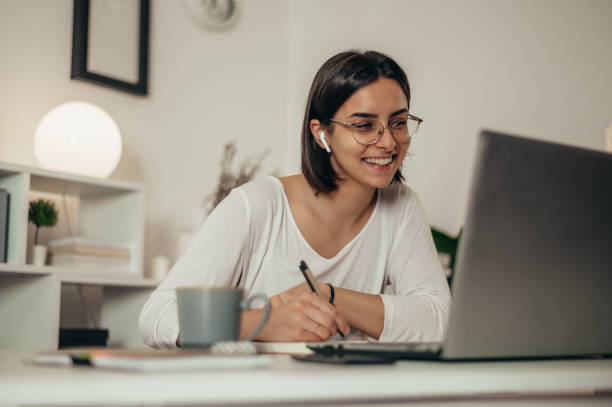 istock Woman writing in a notebook and using a laptop while working from home 1355065713