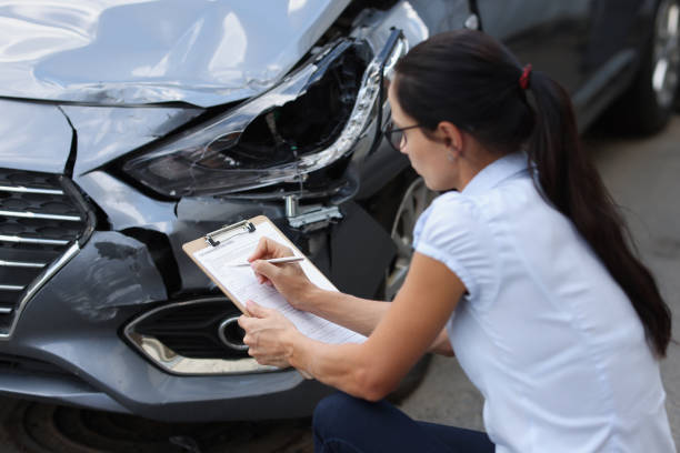 istock Young woman agent sitting near broken car and writing information into documents 1355067342
