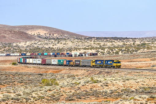 Wirrappa, Australia - Oct 3, 2021: Snake-like in the desert: twin GE diesel locomotives NR23-NR118 speed Pacific National's 7SP3 (Sydney to Perth) express intermodal freight service, round the spectacular serpentine curves at Wirrappa near Pimba in outback northern South Australia.