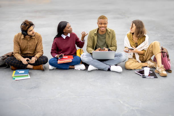 istock Students sitting and using smartphones on asphalt 1355068418