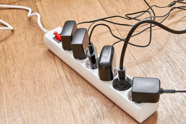 istock Electrical power strip overloaded with multiple electrical cords plugged in. Many plugs plugged into electric power bar 1355068572