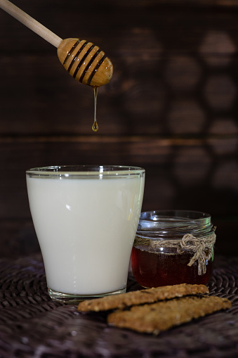 Adding honey to milk at a wooden table, close-up. Oatmeal cookies