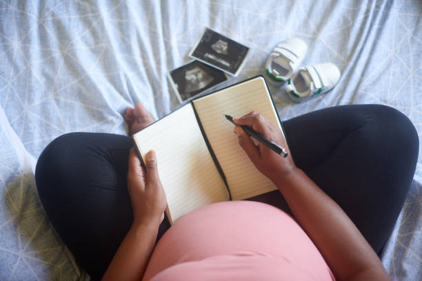 toma de ángulo alto de una mujer embarazada irreconocible escribiendo en su diario mientras está sentada en su cama - diary writing women human hand fotografías e imágenes de stock