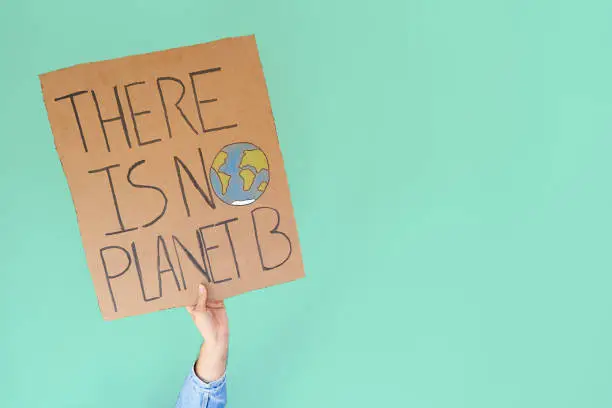 Photo of Stop climate change concept. Hand with denim jacket holding a there is no planet b cardboard sign over turquoise background with copy space