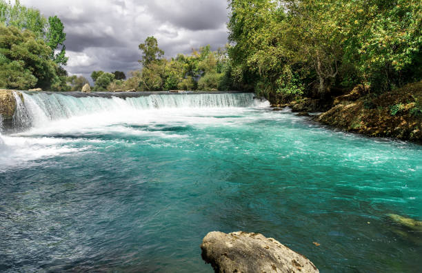 Amazing fast flowing rocky stream with small waterfall cascade flows into the turquoise pond. Picturesque mountain waterfall landscape. Beautiful natural background for your design.