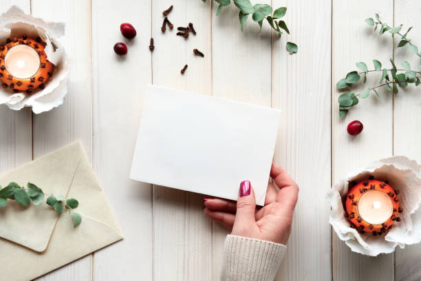 istock Blank postcard in hand. Winter holiday greeting card mockup. Eucalyptus, tea light in pomander ball 1355078406